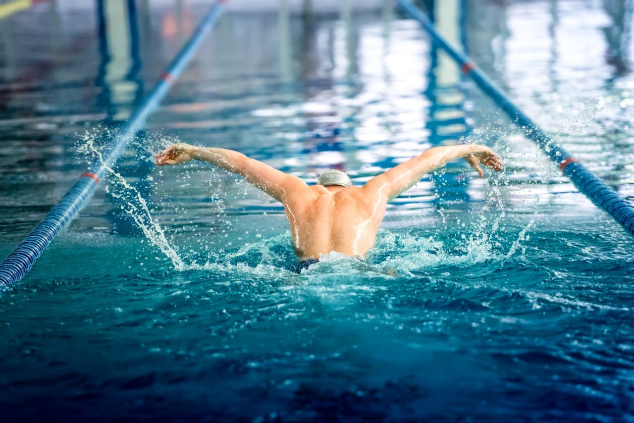 Male swimmer performing the butterfly stroke at indoor swimming competition